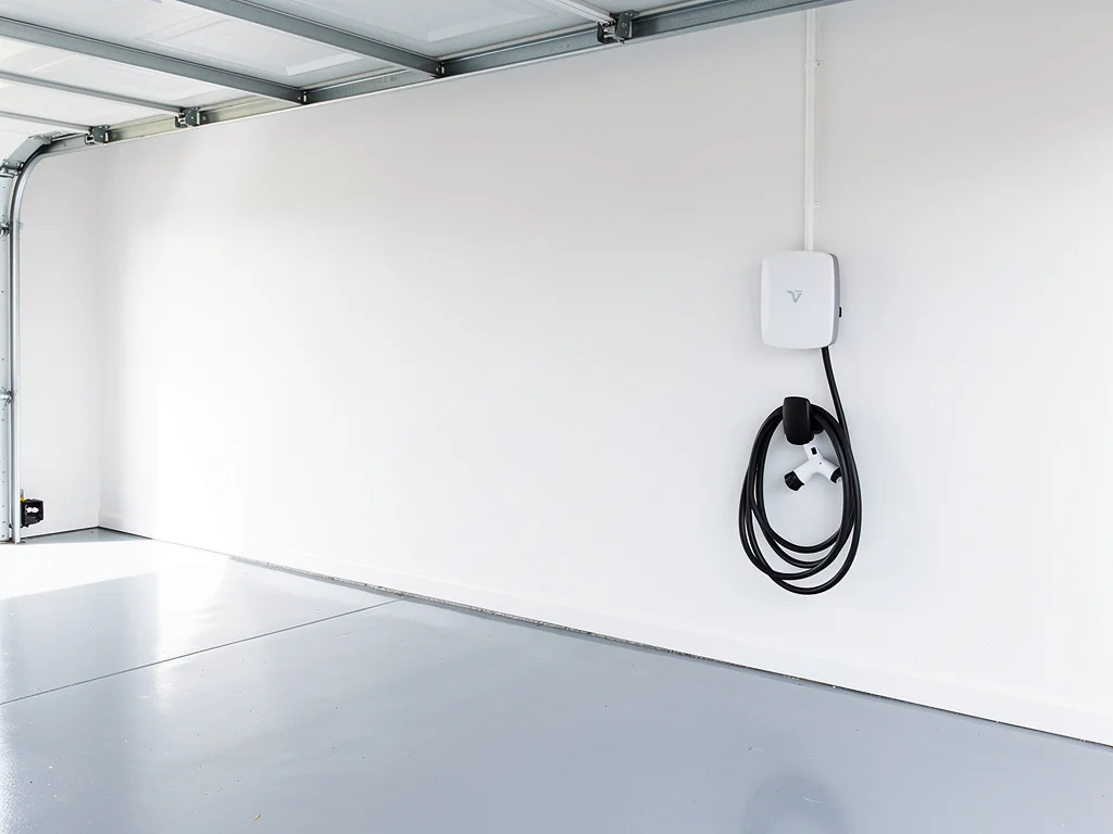 Wallbox blanche fixée au mur d'un garage résidentiel, câble lové sur son support